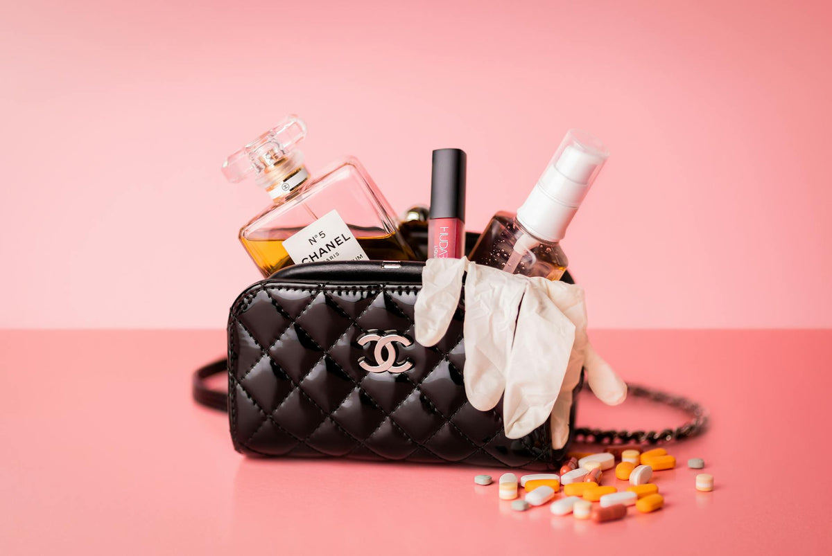 Chanel bag featuring perfume, gloves, and medicines on a pink surface for a mix of luxury and health